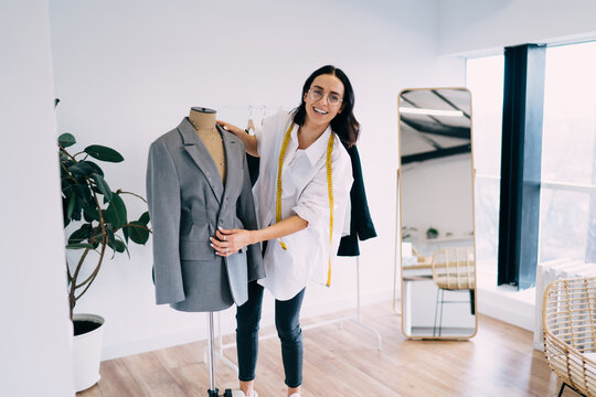 Cheerful seamstress standing near mannequin with jacket