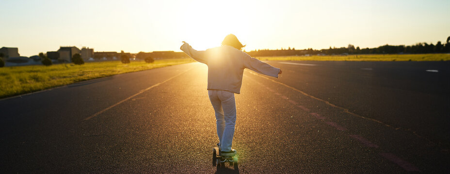 Teen girl feeling happy on longboard. Happy young skater riding her skateboard with hands spread sideways, feeling freedom, going towards the sun