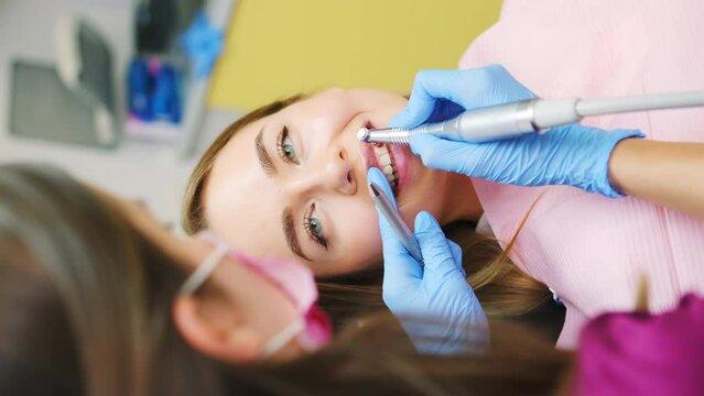 A dentist is performing a teeth grinding procedure on a lovely woman to enhance her smile, vertical video