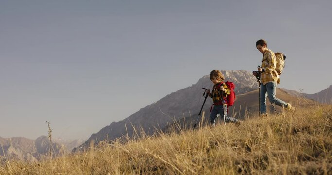 Mother and child conquer mountain, trekking poles backpacks. Beauty in nature, unforgettable journey, golden hues of fall morning adventurous spirit, mountain trail autumn hike, cinematic, family trip