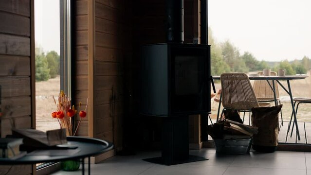 Shot of a cozy living room in a wooden house with panoramic windows overlooking pine trees with fireplace and beams for lighting it