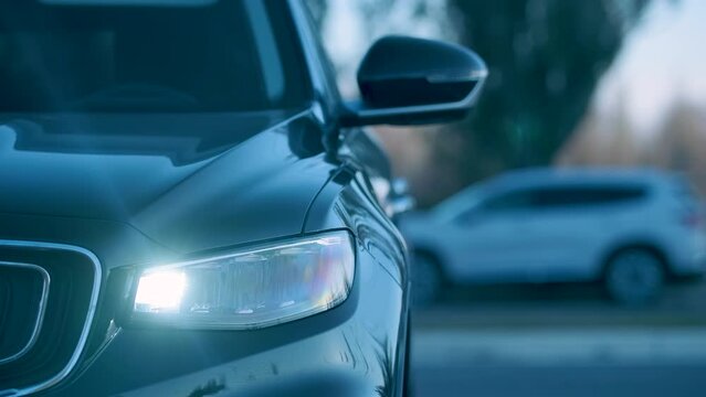 Starting the engine is accompanied by the automatic folding of the side rear-view mirrors and the lighting of the LED front optics of a modern black car in the evening