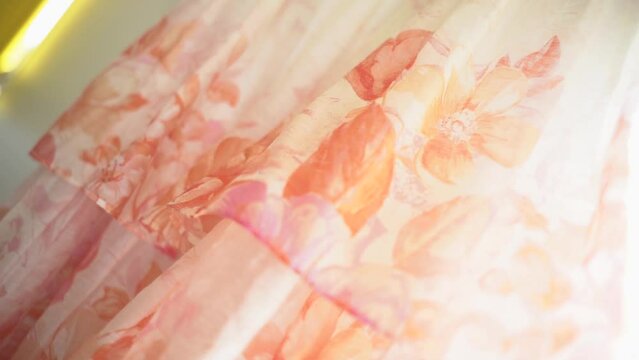 Pink dress with flowery pattern hanging nearby window before wedding in New Zealand