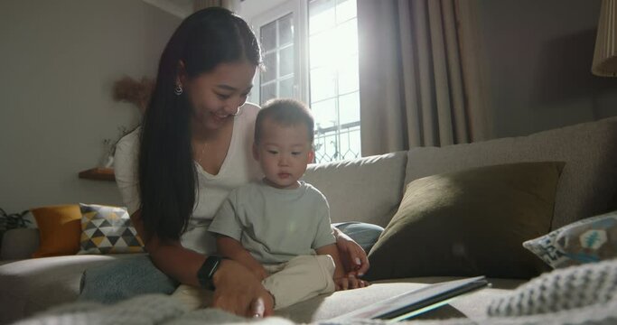 Asian mom and toddler spending time together. Multiethnic asian mom smiling wide happy flipping through book, reading fairy tale, looking at pictures in book. Little boy interested in book fairy tale