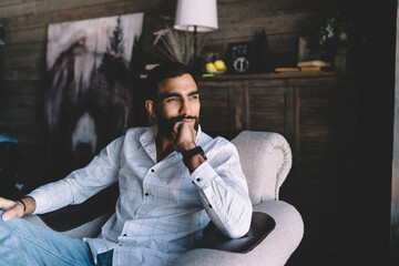 Thoughtful young man sitting on sofa in living room