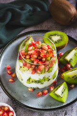 Tropical fruit kiwi, fresh yogurt and pomegranate seeds in a glass vertical view
