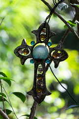 Cruz metalica, con cuentas y piedras de cuarzo, colgada sobre un árbol.