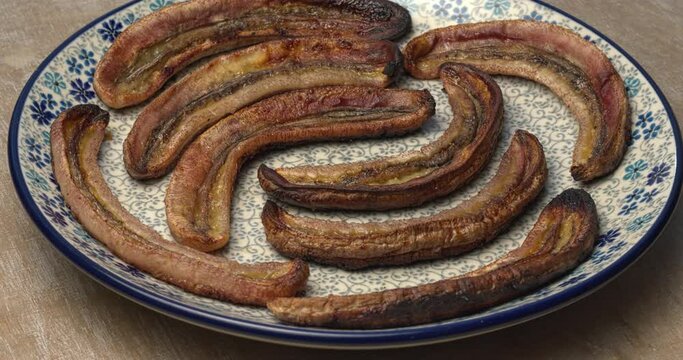 Peeled, cut lengthways, and long roasted bananas on a plate. Table spin. 