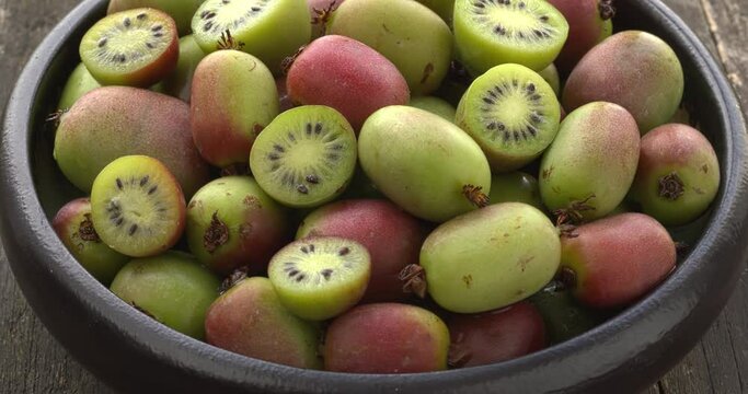 Hardy kiwi fruit (Actinidia arguta) in a bowl. Ripe and raw mini kiwi fruit. Table spin.