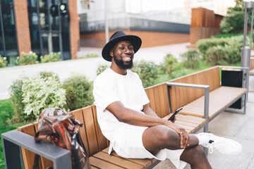 Positive black man using smartphone on bench