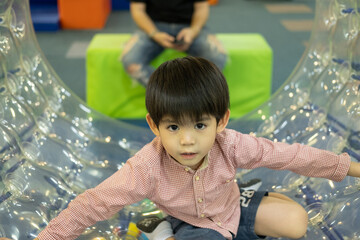 A little Asian boy is playing with a giant, rolling ball with holes.