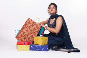 Portrait of young Indian woman or girl in a traditional dress sitting with shopping bags and gifts during festival isolated over white background