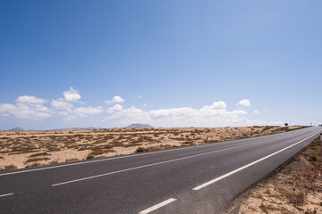 Desert landscape of white sand and desert shrubs. Asphalt road, mountains in the background. Sky with big white clouds. Lanzarote, Canary Islands, Spain.