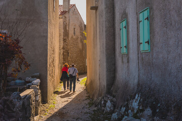 Two older tourists are strolling through the town of lubenice, a beautiful small croatian town on the island of cres, with all its small and narrow streets. - obrazy, fototapety, plakaty