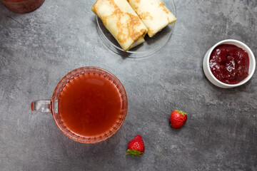 a cup of fruit tea, pancakes with berry filling and strawberries on a dark gray background. top view.