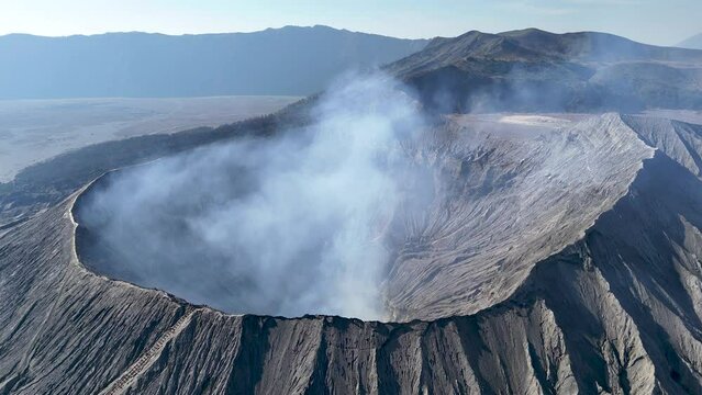 Aerial 4K footage of the Bromo volcano crater caldera with smoke coming. An active volcano in Tengger Semeru National Park in East Java, Indonesia.