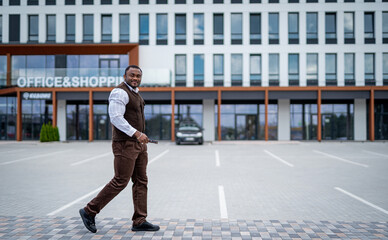 Fototapeta na wymiar Man Walking Across Busy Parking Lot in Front of Modern Office Building. A man walking across a parking lot in front of a building