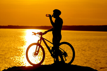 Fototapeta premium A man standing next to a bike on top of a rock. Man Surrounded by Nature's Beauty