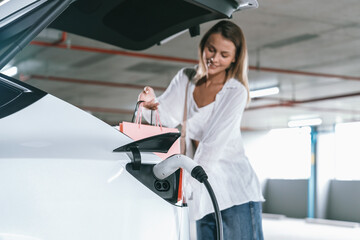 Young woman travel with EV electric car to shopping center parking lot charging in downtown city...