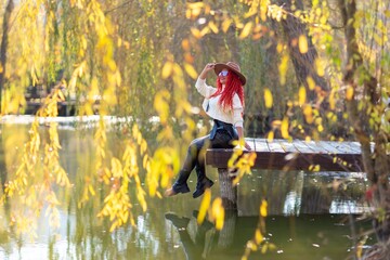 Autumn lake woman. In autumn, she sits by the pond on a wooden pier and admires nature with red...
