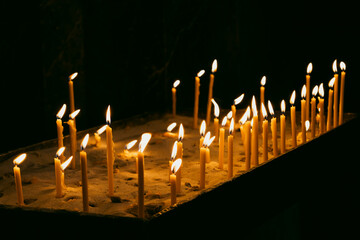 Many burning tall wax candles with bokeh light background. Catholic or Orthodox church. Flame of candles in the dark sacred interior of the temple. Religious tradition. Prayer and Christian Faith