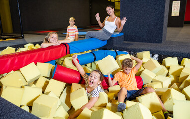 Playful happy children friends spending time together having fight with foam cubes, throwing them at each other in indoor kids entertainment centrer