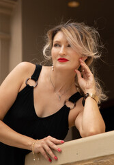 A beautiful girl in a black dress poses on the stairs against the background of beigeand blue  