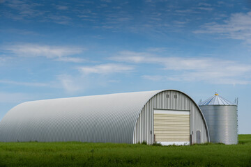 Farmyard quonset used for storing agriculture machinery overlooking a grain silo on the Canadian prairies in Kneehole Country Alberta Canada.