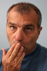 Fototapeta premium Close up portrait of adult male face holding his hand in front of his mouth in expression of surprise or to say to other to stop talking.