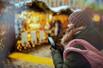 modern woman at christmas fair in city using smartphone