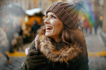 happy woman in green coat and brown hat at winter fair in city