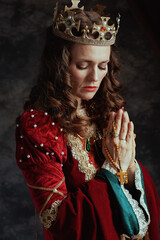 medieval queen in red dress with rosary and crown praying