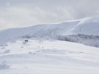 Winter mountain landscape. Mountain peaks covered with snow. View from Mala Rawka to Wielka Rawka. three tourists walking along a snow-covered trail.  Bieszczady Mountains. Poland