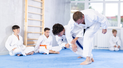 Karate master demonstrating basic martial art skills, strikes, kicks and throws to group of novice...