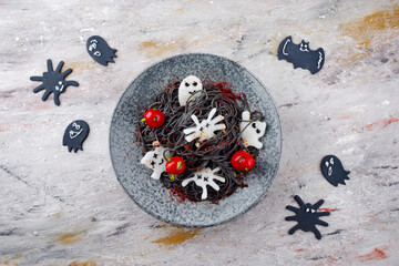 Traditioneller Halloween Tintenfisch Spaghetti mit Dracula Spinnen, Fledermäuse und Bluttropfen Tomaten serviert als Draufsicht in einem Nordic Design Teller