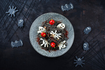 Traditioneller Halloween Tintenfisch Spaghetti mit Dracula Spinnen, Fledermäuse und Bluttropfen Tomaten serviert als Draufsicht in einem Nordic Design Teller