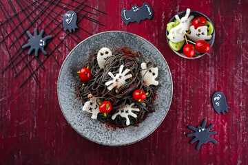 Traditioneller Halloween Tintenfisch Spaghetti mit Dracula Spinnen, Fledermäuse und Bluttropfen Tomaten serviert als Draufsicht in einem Nordic Design Teller