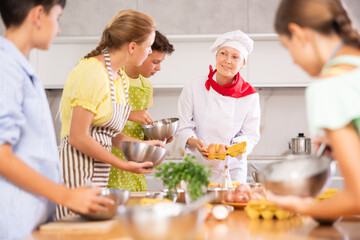 Fototapeta na wymiar Adult woman cook in uniform teaches group of children how to cook dish