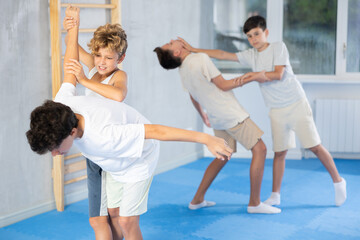 Teenage students attending self-defense classes at training center. Boy applying armlock technique to opponent in sparring under careful supervision of instructor..