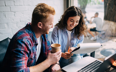 Cheerful colleagues working on laptop and clipboard in cafe