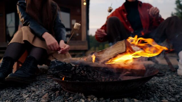 Close-up shot of several people roasting marshmallows on fire on a wood fire in nature during sunset