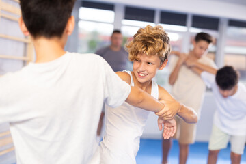 Fototapeta premium Focused kids in pair exercising self-defense movements during group class in modern sports studio, closeup