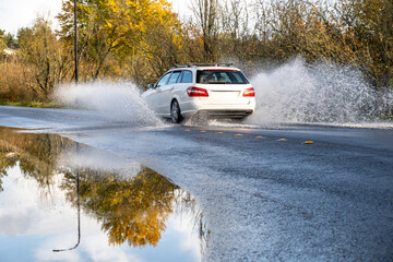 After the storm, white car splashing through rainwater flooding over a residential street on a...