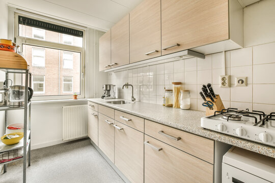 a small kitchen with white appliances and wood cabinetd cupboards on the left side of the photo is an open window