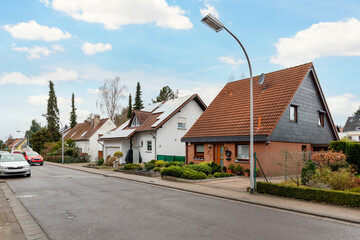 City street of single-family modern houses Germany against blue sky. German suburban small town residential area with row eco sustainable life building neighborhood suburb. Urban car parking driveway - obrazy, fototapety, plakaty