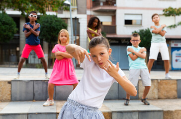 Confident preteen b-girl dancing with group of friends on city street. Urban lifestyle. Hip-hop generation..