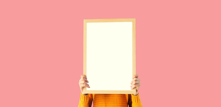 Portrait of woman holding and showing blank a photo frame mockup on pink studio background