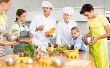 In restaurant kitchen, two experienced chefs, man and woman, conduct cooking courses for children