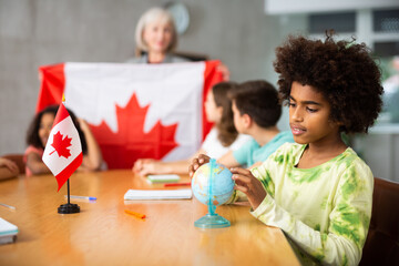 at evening geography lesson, elderly teacher tells attentive students about Canada
