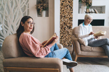 Obraz premium Smiling mature ethnic woman sitting with book in living room at home